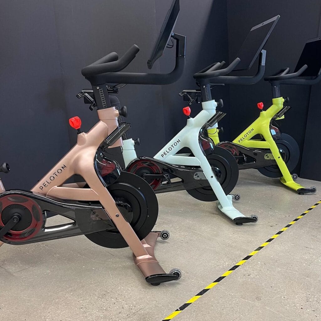 Peloton bikes shown in different colors: rose gold, neon yellow, and sky / light blue.